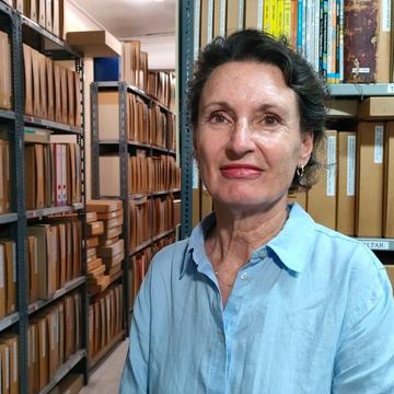 Photo of OOC DTP Director Professor Laura Wright, white woman in a blue shirt standing in front of bookshelves