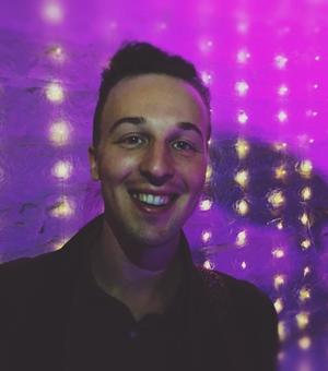 Photo of Daniel Brew, smiling man against shining magenta background